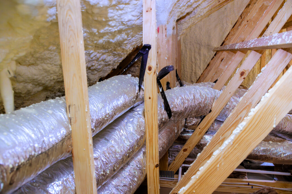 Ducts in an attic surrounded by insulation foam.